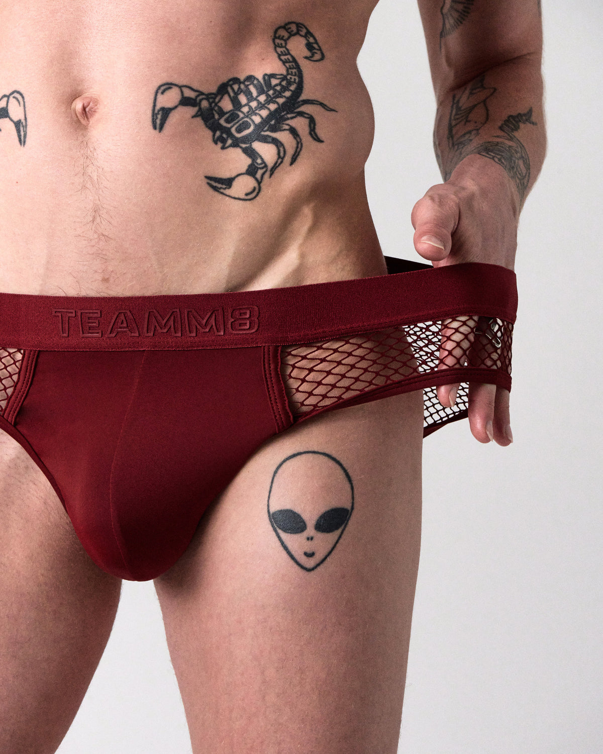 Edge Net Brief en Maroon, acercamiento frontal mientras el modelo jala la pretina para mostrar el costado de malla