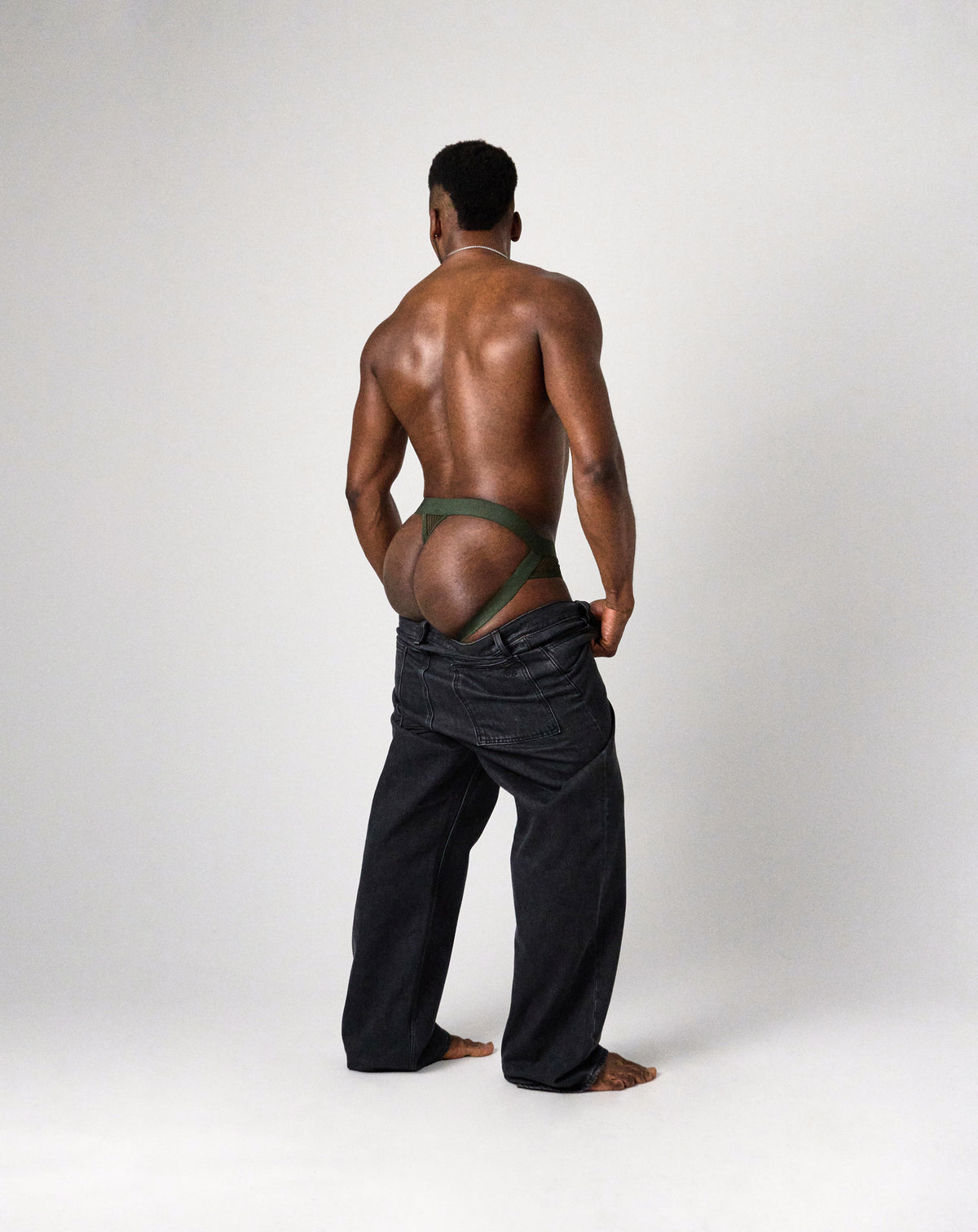 Edge Net Jock/Thong in Forest, back view on model with black jeans pulled down to show the straps