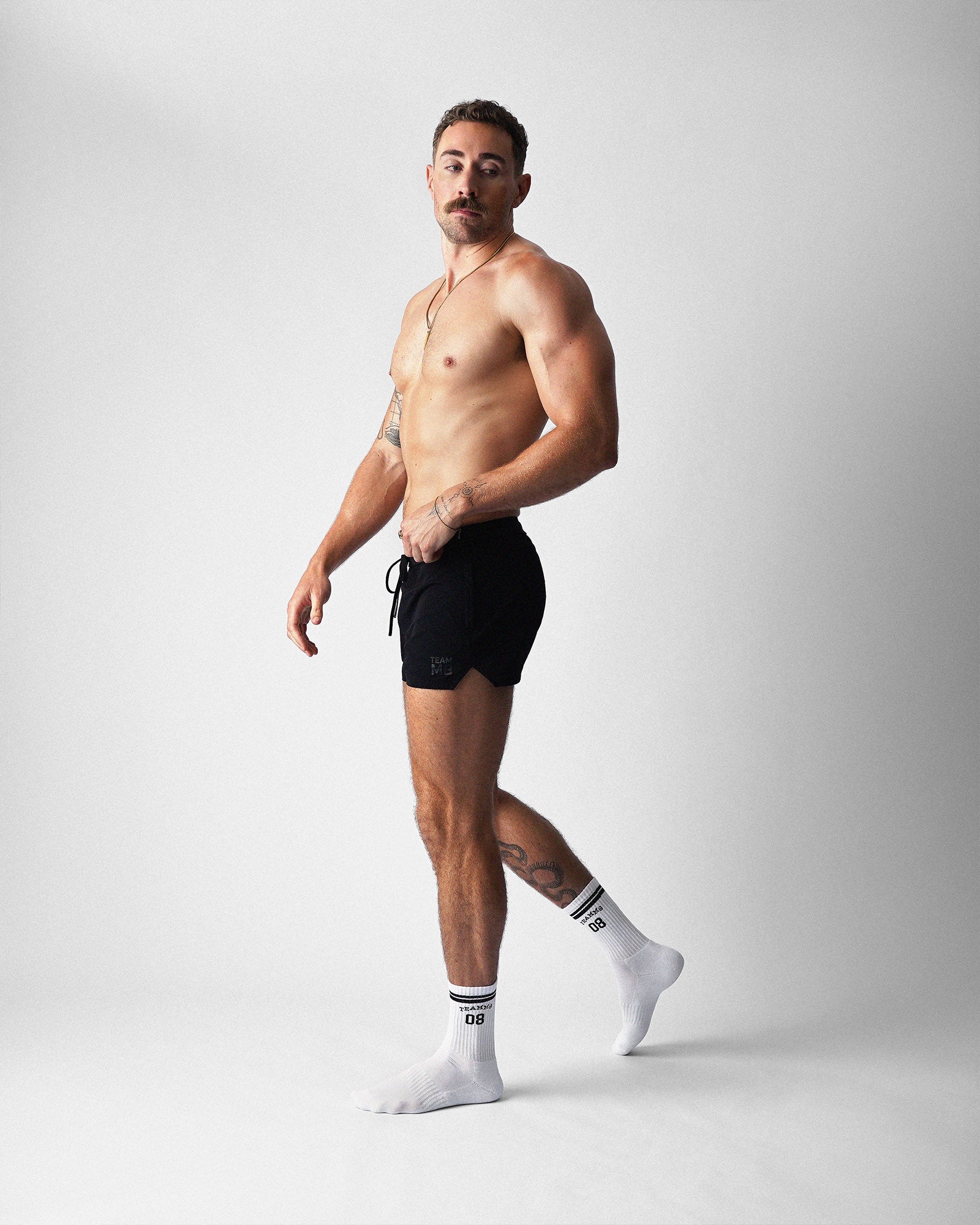 Man wearing black athletic shorts and white socks on a light gray background